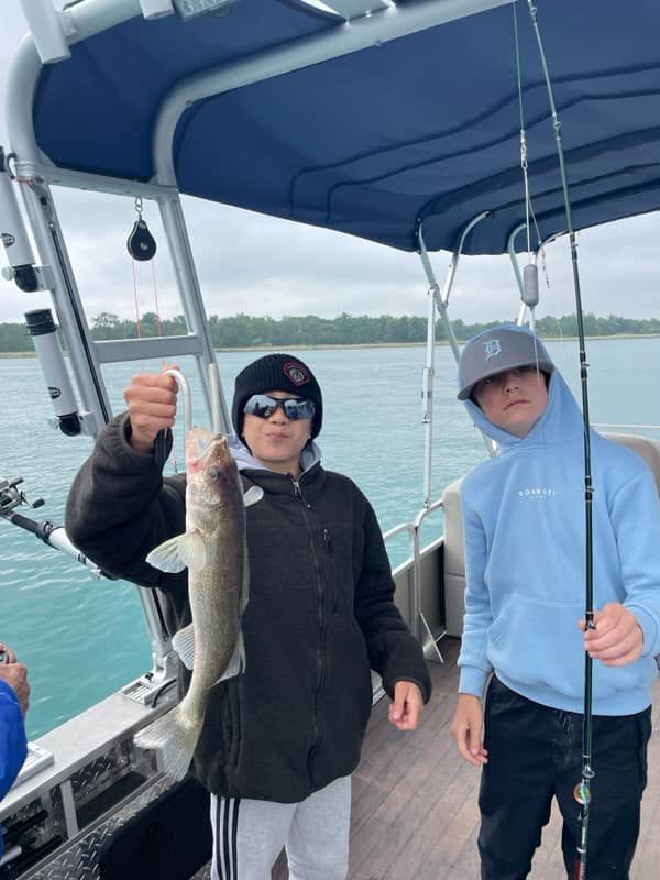 Two boys are fishing on a boat and one of them is holding a fish.