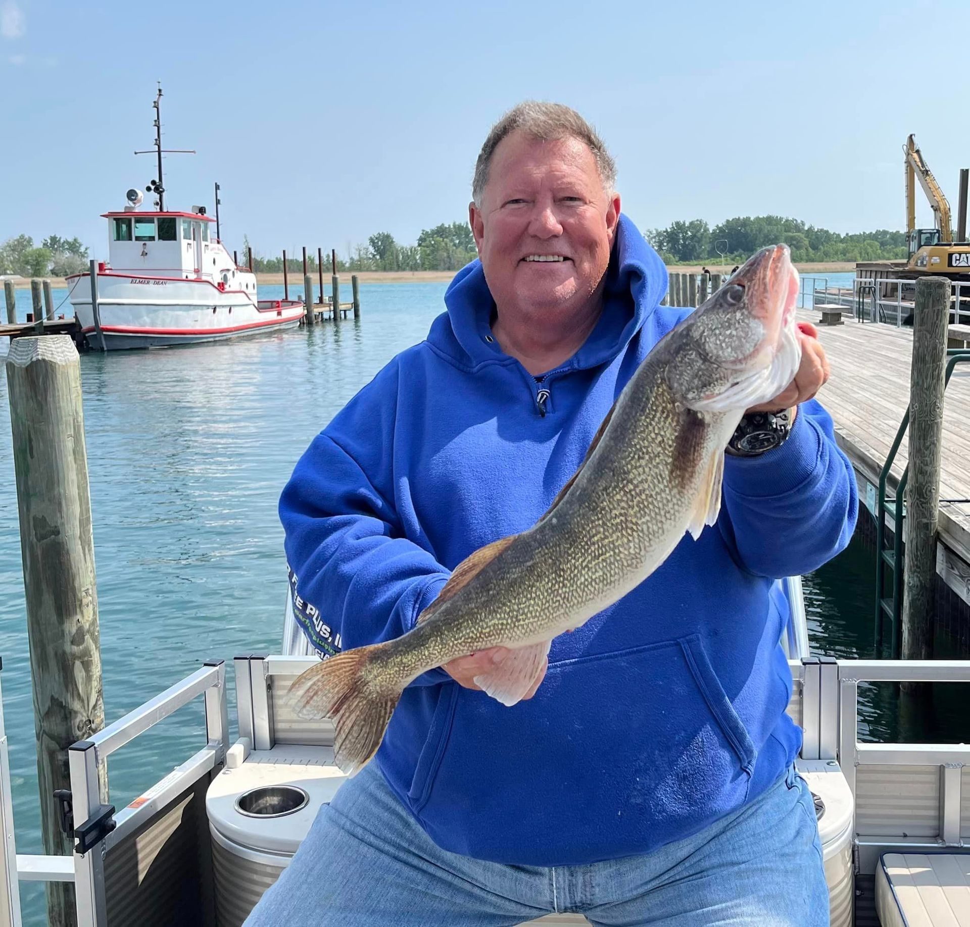 A man in a blue hoodie is holding a large fish