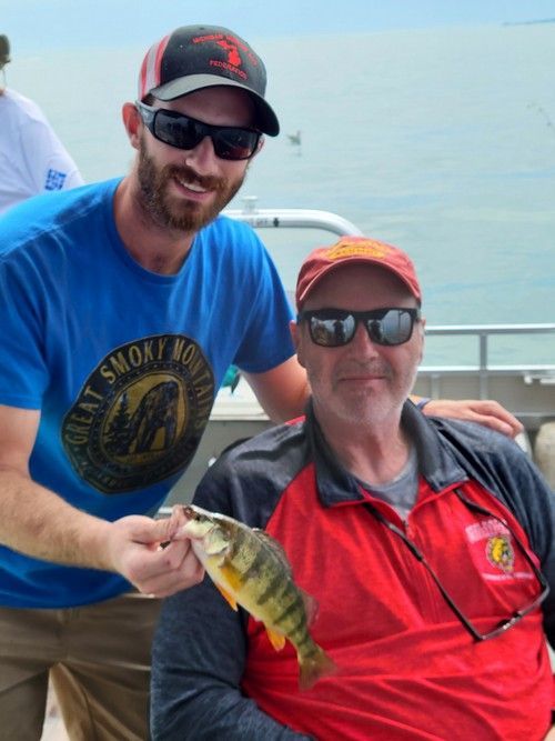 A man in a lake smoky boat shirt holds a fish next to another man.