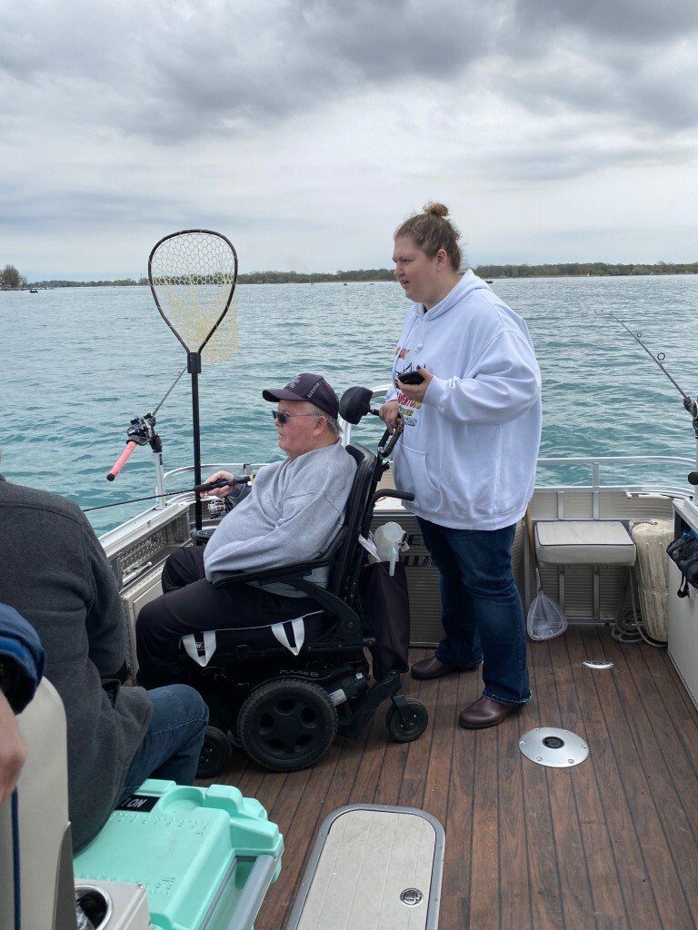 A man in a wheelchair is fishing on a boat with a woman standing next to him.