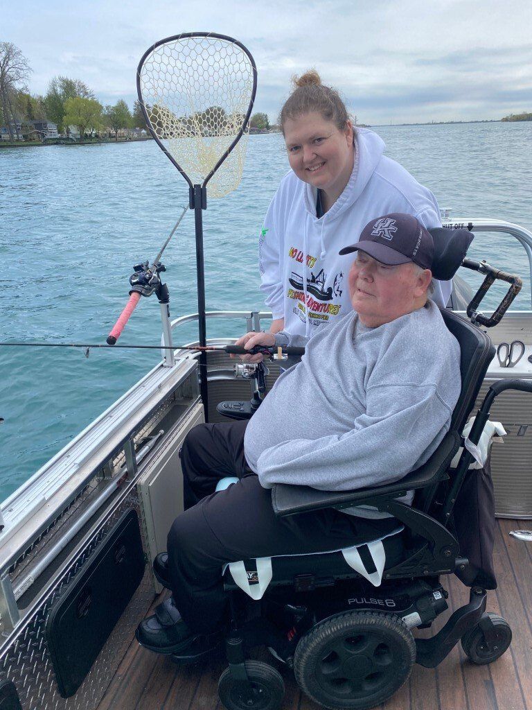 A man in a wheelchair is fishing on a boat with a woman.
