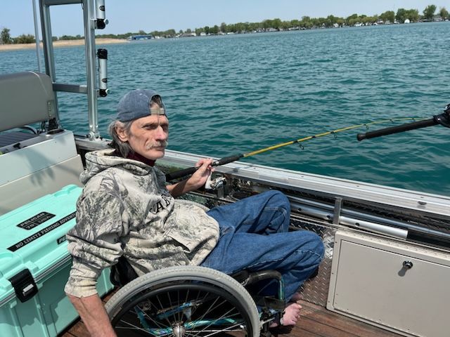 A man in a wheelchair is fishing on a boat.