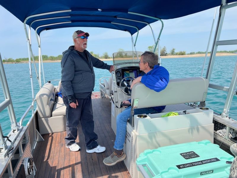 Two men are standing on a boat in the water talking to each other.