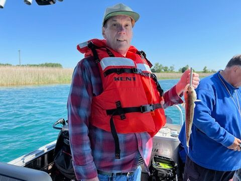 A man wearing an orange life vest is holding a fish on a boat.