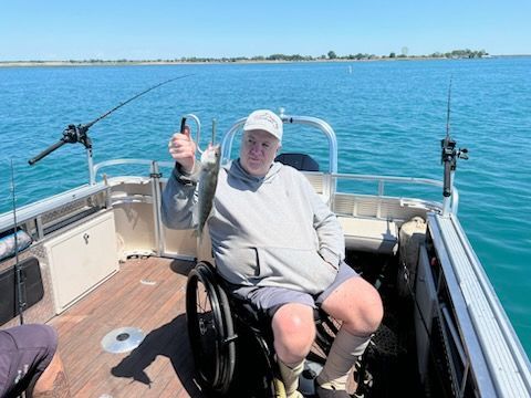 A man in a wheelchair is sitting on a boat holding a fish.