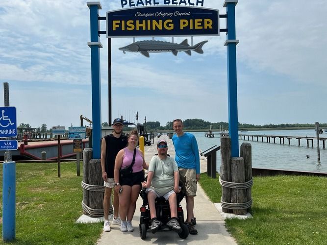 A group of people are posing for a picture in front of a fishing pier sign.