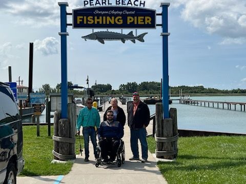 A man in a wheelchair is standing in front of a fishing pier sign.