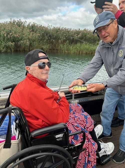 A man in a wheelchair is being given a fish by another man on a boat.