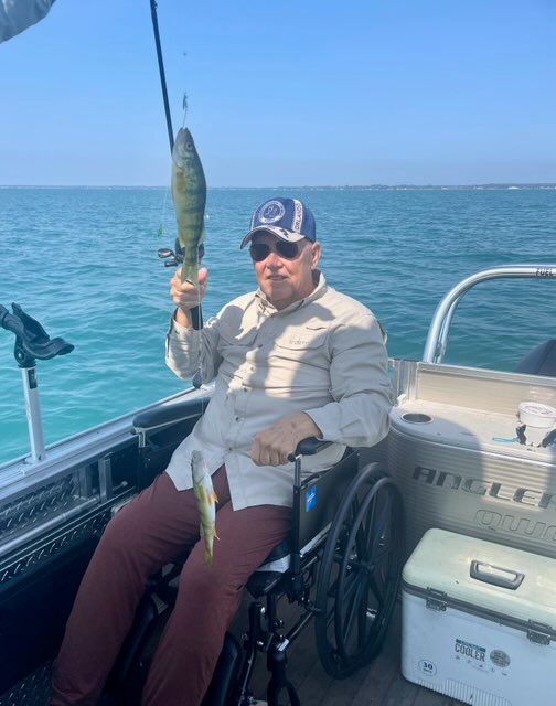 A man in a wheelchair is holding a fish on a boat.
