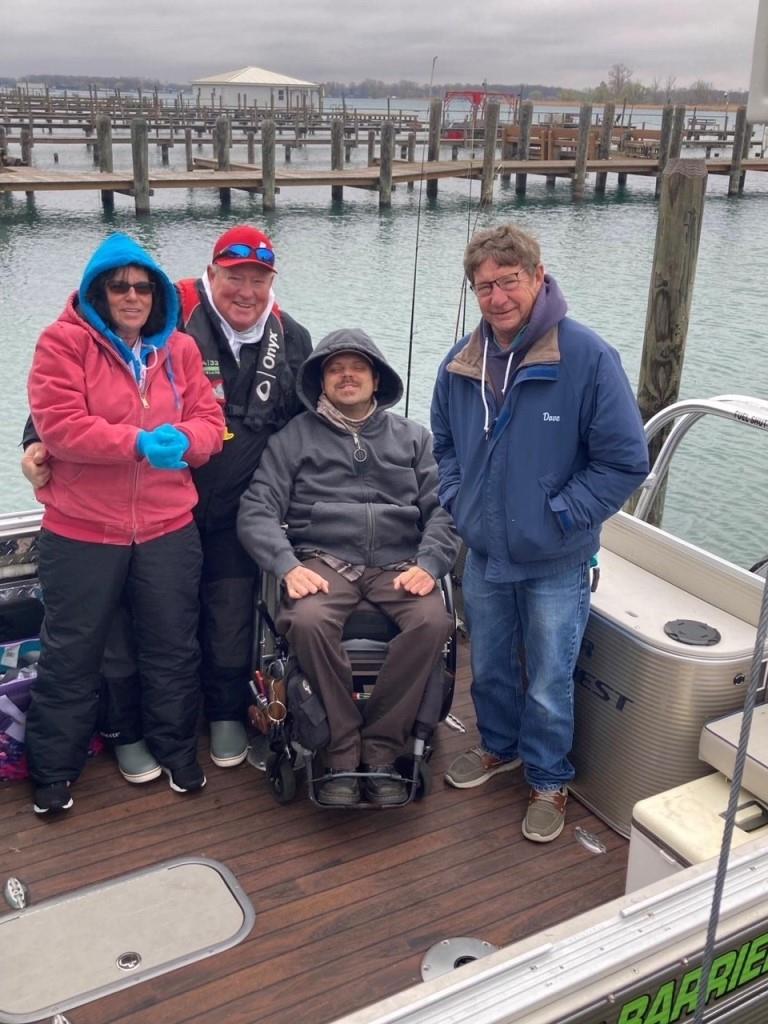A group of people are standing on a boat with a man in a wheelchair.