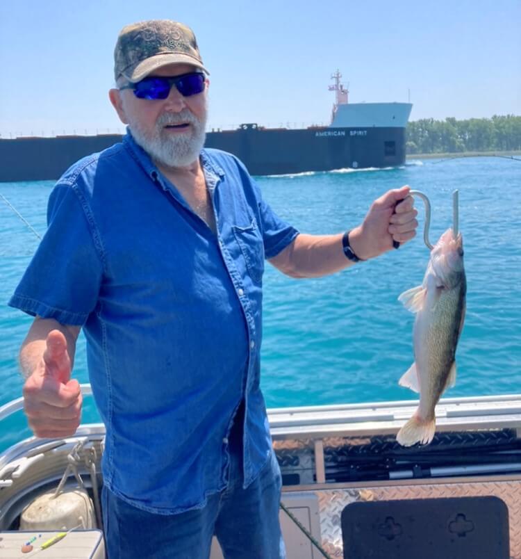 A man in a blue shirt is holding a fish and giving a thumbs up