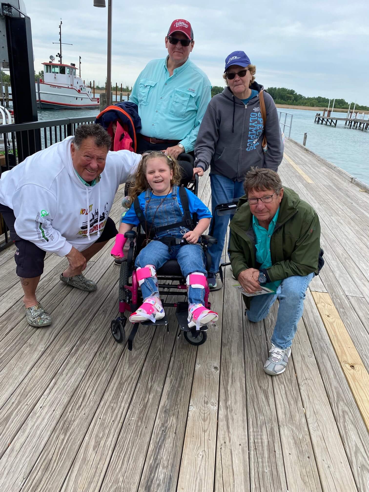 A group of people are posing for a picture on a pier with a girl in a wheelchair.