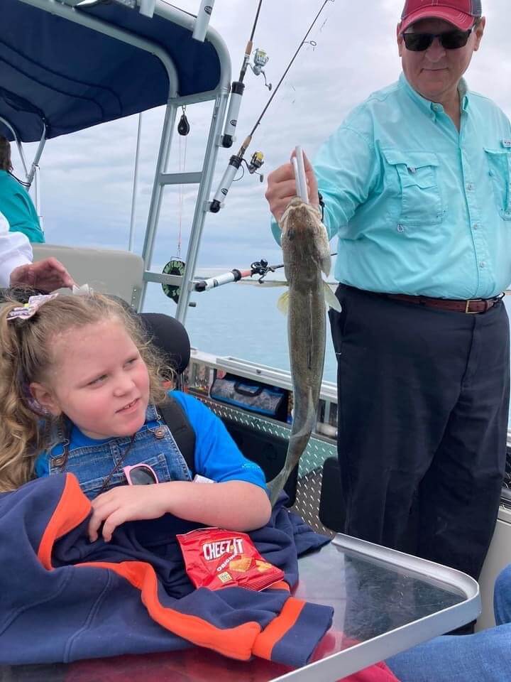A little girl is sitting on a boat while a man holds a fish.