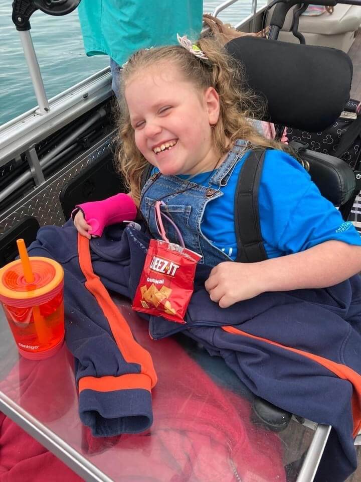 A little girl is sitting on a boat holding a bag of chips.