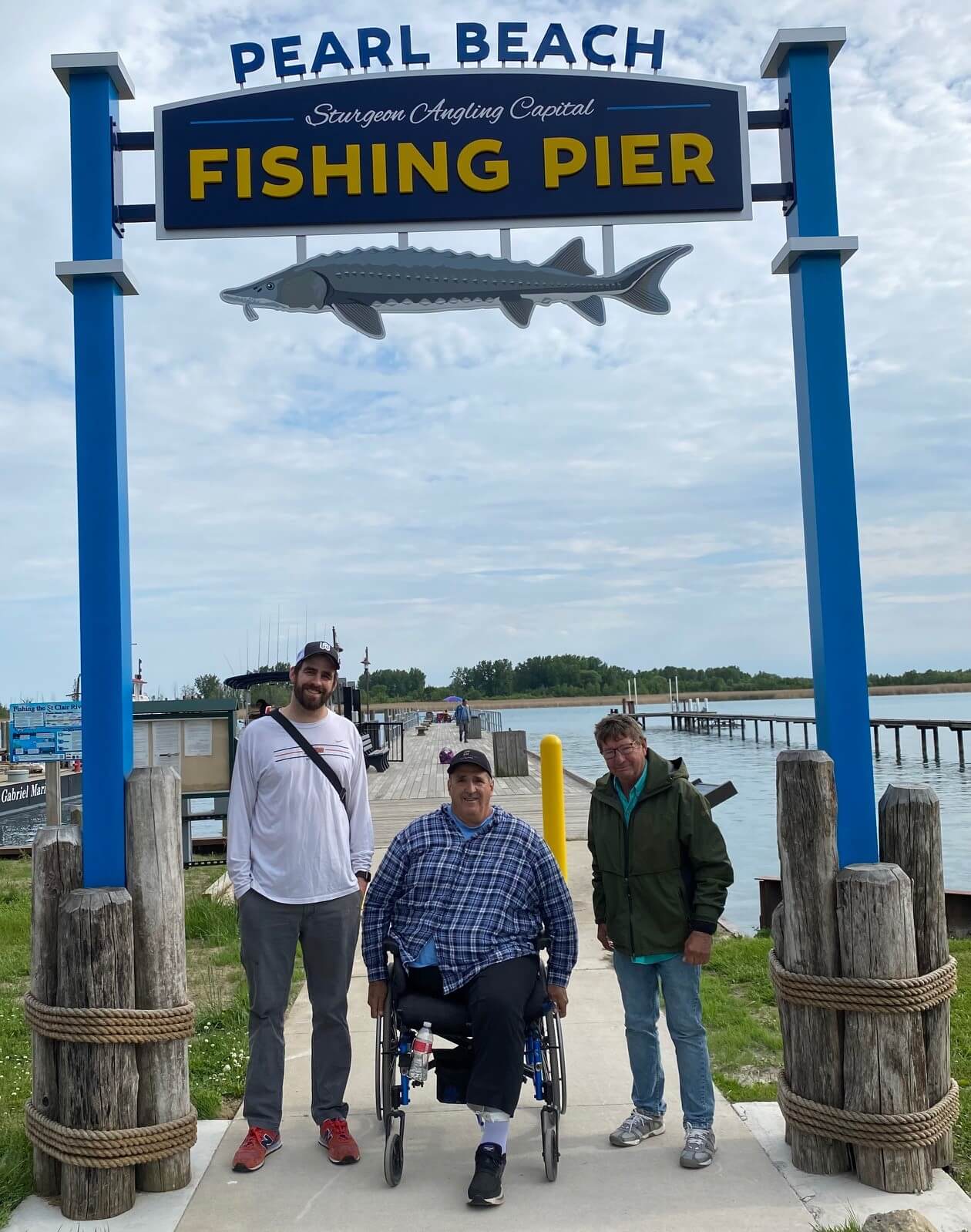 Three men are standing under a sign that says pearl beach fishing pier