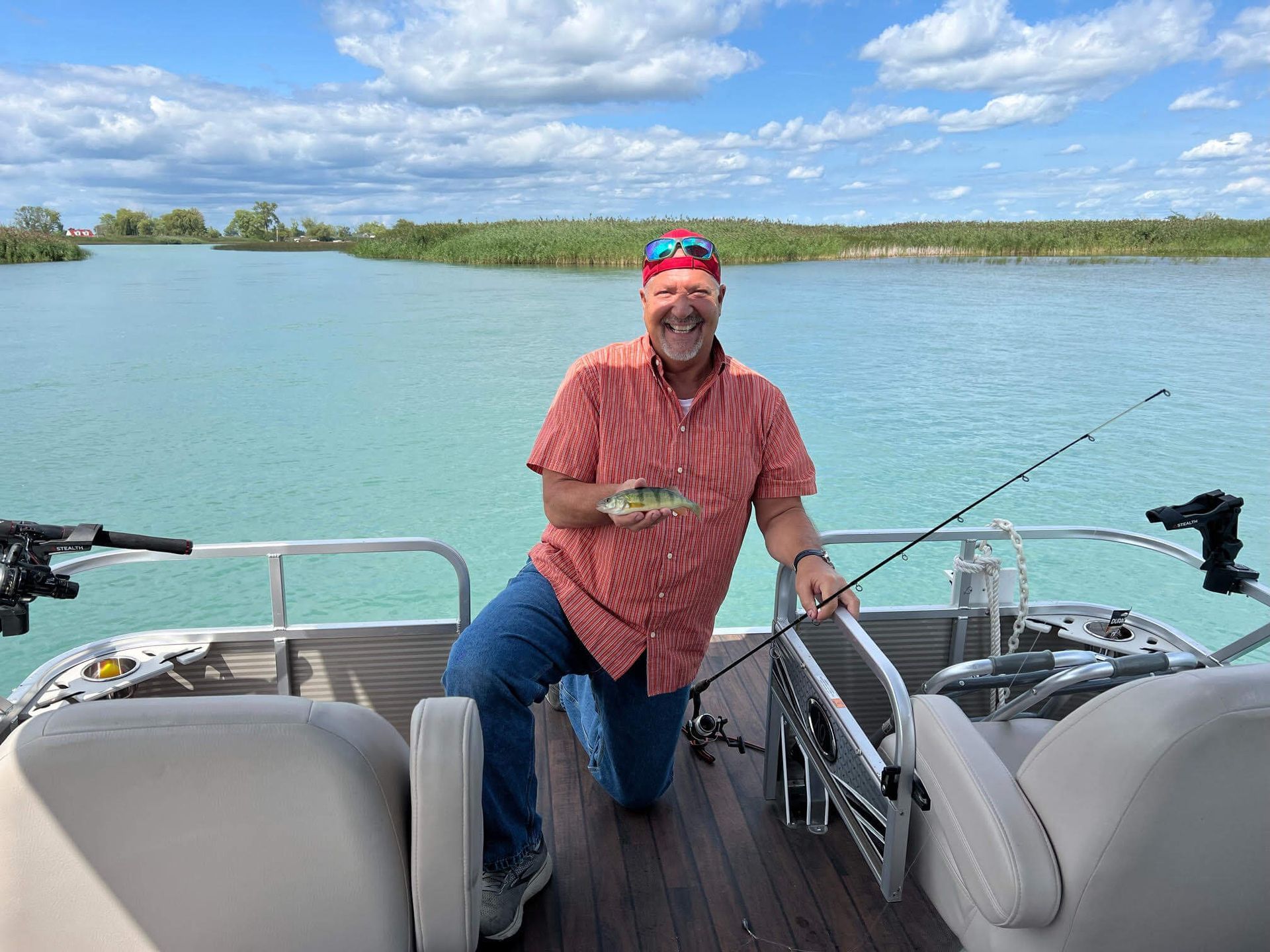 A man is kneeling on a pontoon boat holding a fishing rod and a fish.