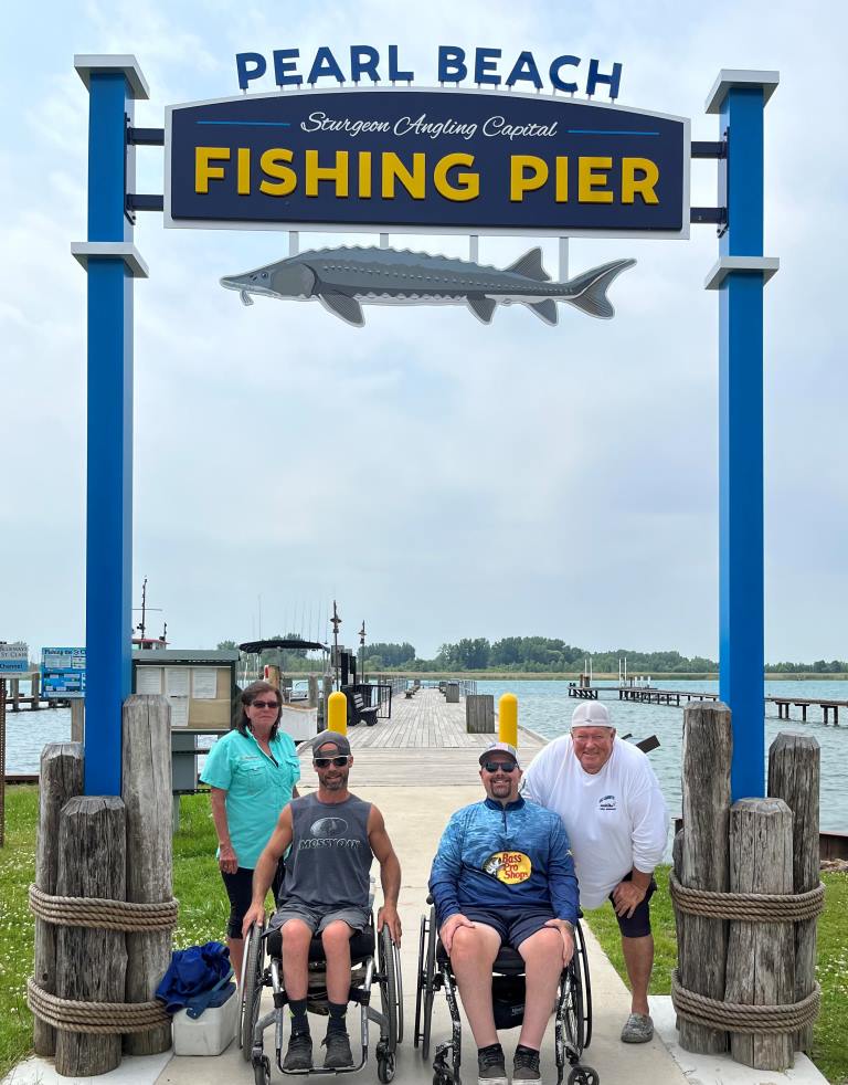 A group of people in wheelchairs are posing for a picture at the pearl beach fishing pier.