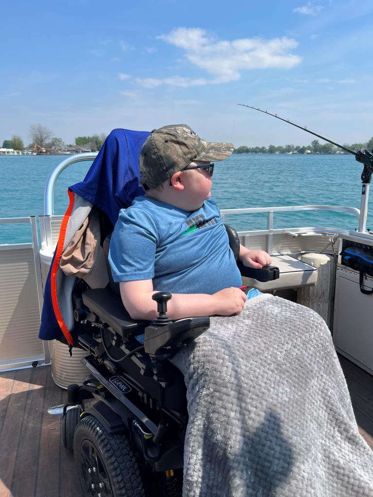 A boy in a wheelchair is fishing on a boat.