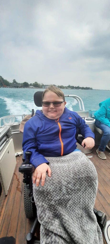 A young boy in a wheelchair is sitting on the deck of a boat.