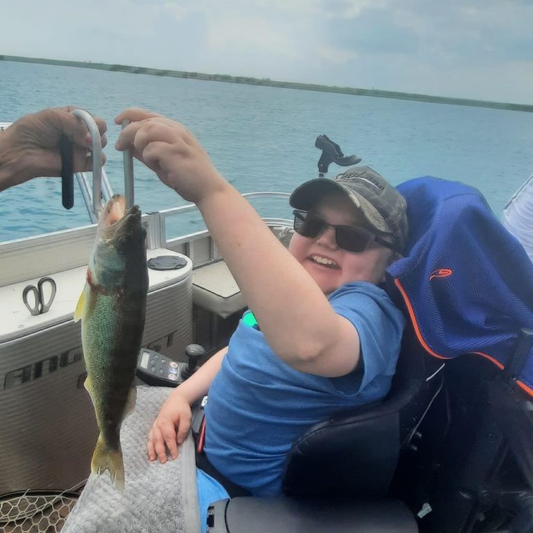 A boy in a wheelchair is holding a fish in his hand