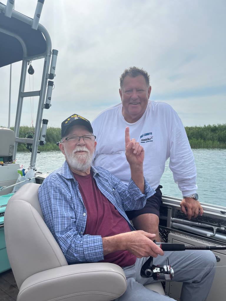 Two men are sitting on a boat holding fishing rods.