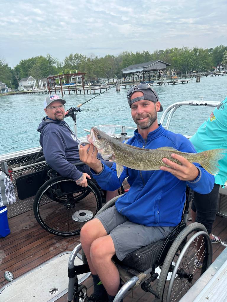 A man in a wheelchair is holding a fish on a boat.