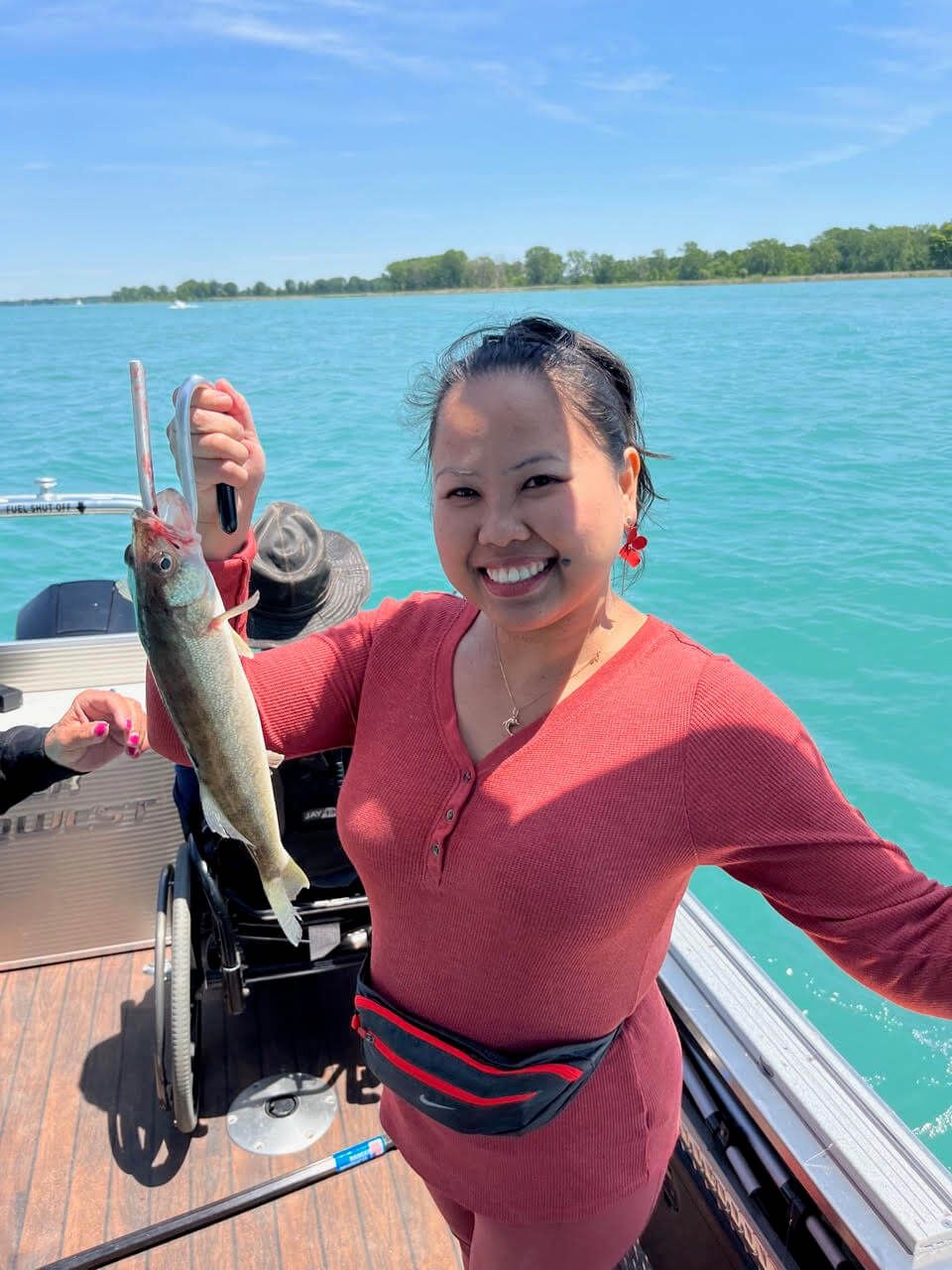 A woman in a wheelchair is holding a fish on a boat.