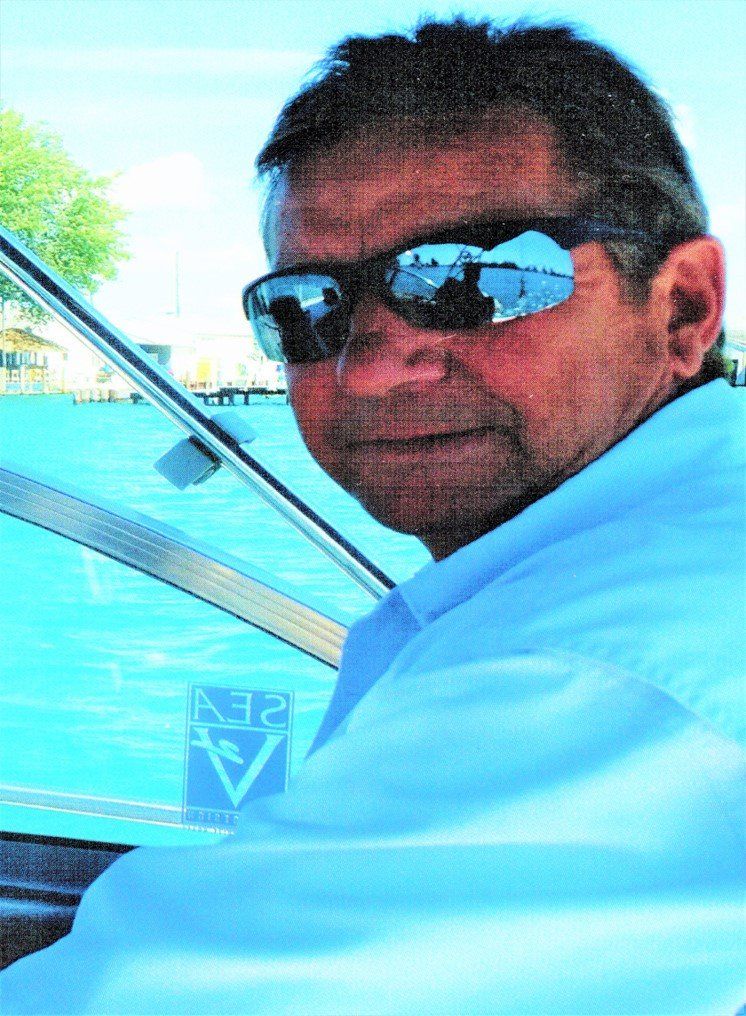 Man in sunglasses at helm of boat, turquoise water, sunny day.