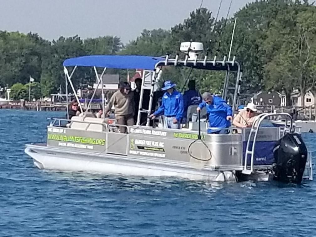 Pontoon boat with people fishing, on water near trees.