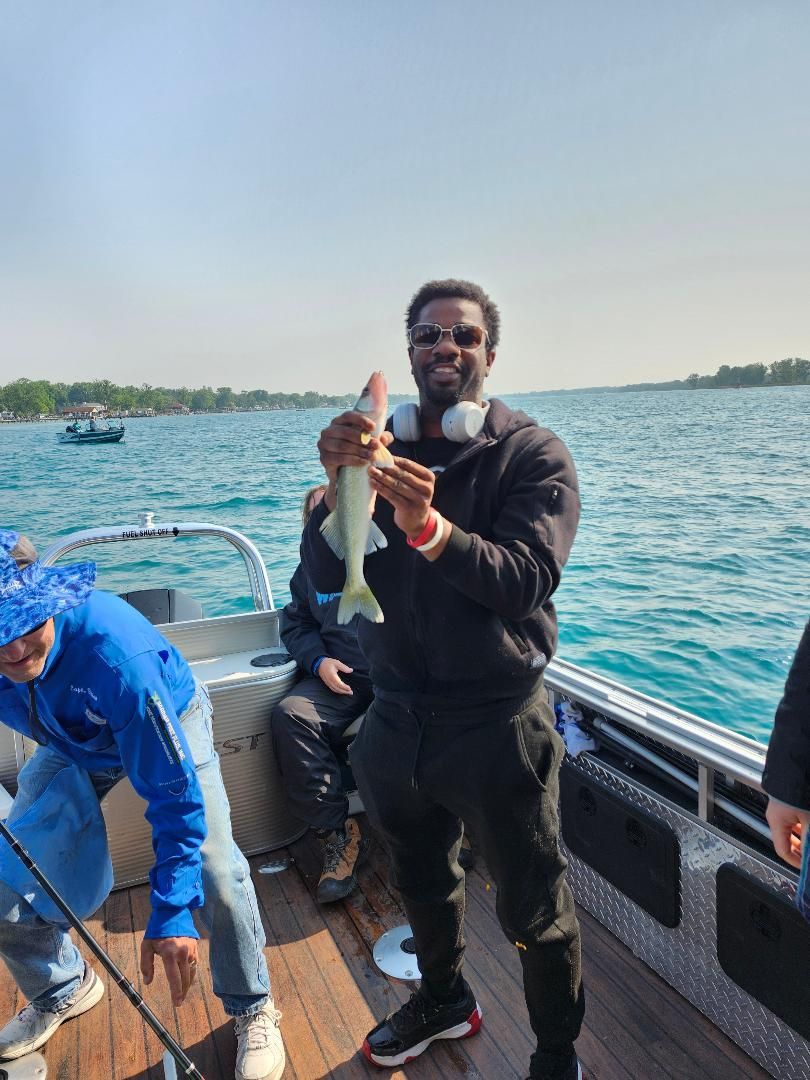 Man on a boat holding a fish, smiling. Blue water and sky in the background.