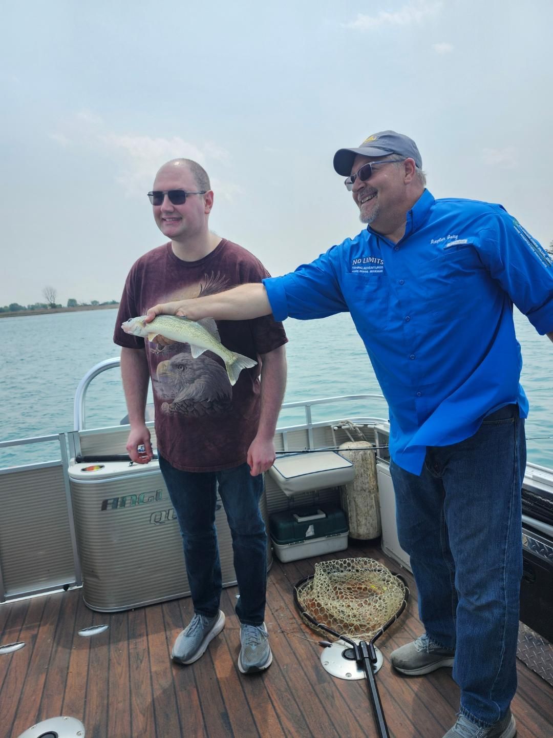 Man holding fish, smiling, on boat with another man wearing sunglasses.