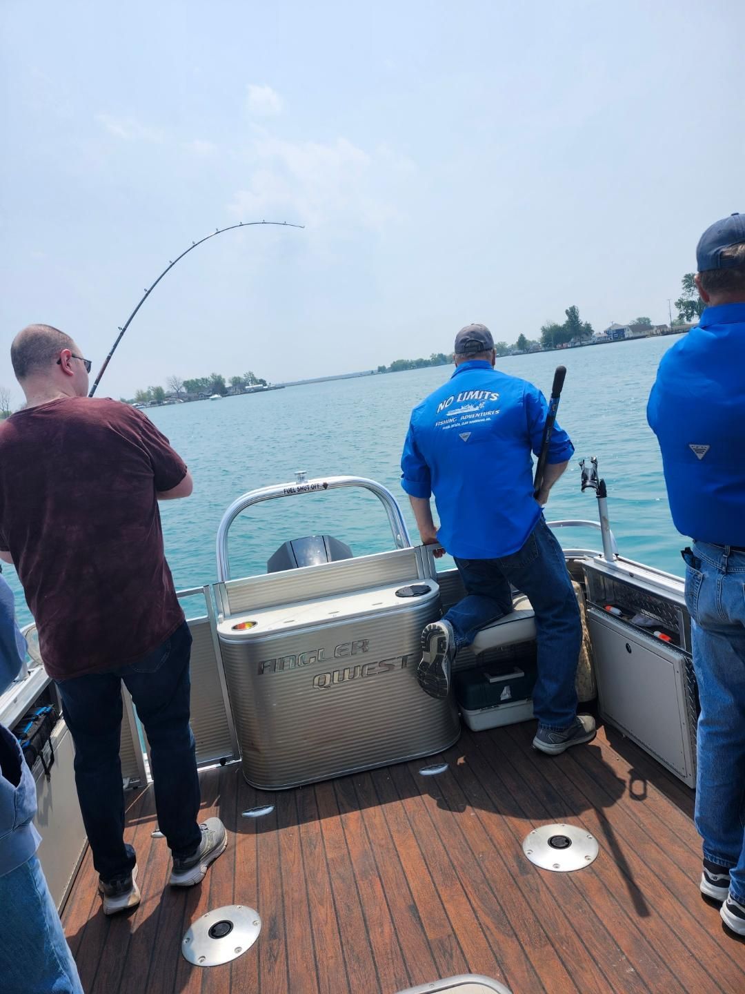 People fishing from a boat on a sunny day. A person is reeling in a fishing rod.