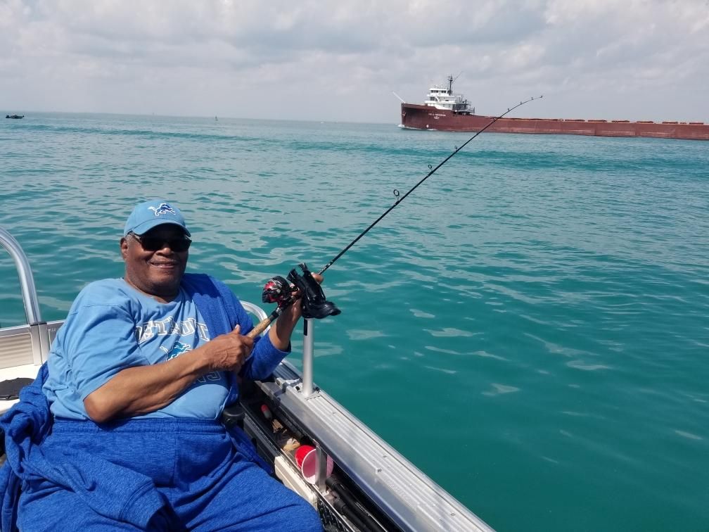 Person fishing from a boat on blue water, a large ship in the distance.
