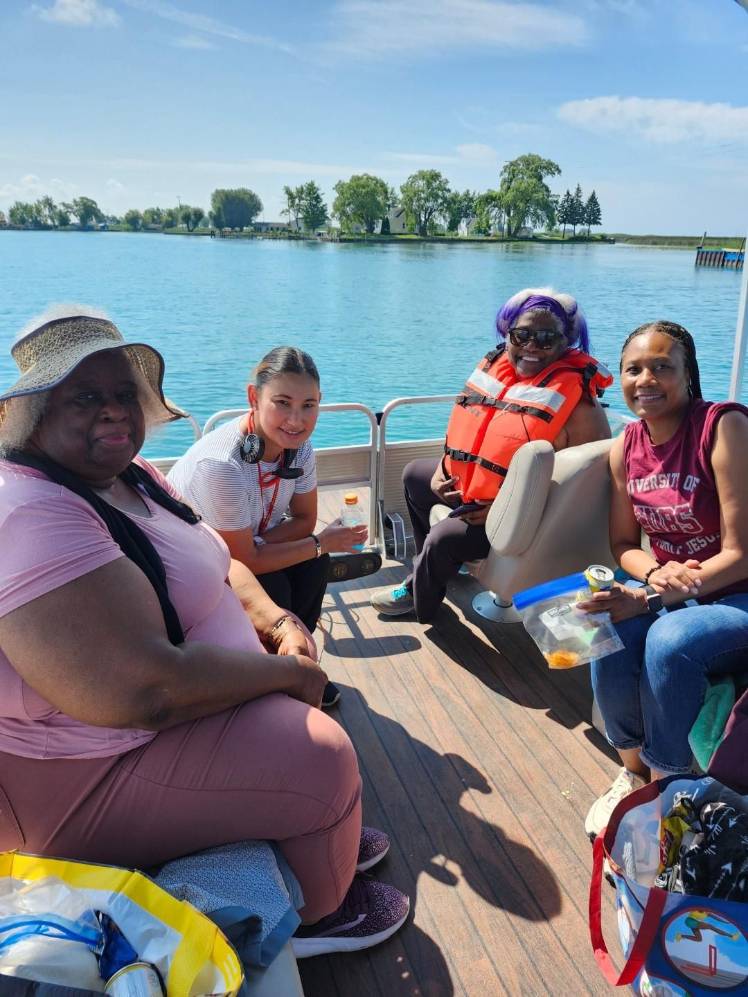 Four people on a boat on a sunny day; blue water, trees in background, one person in life vest.
