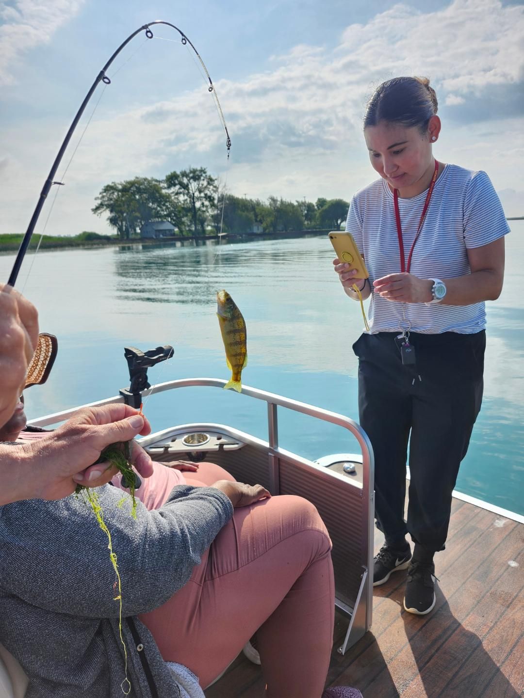 Woman assisting a person fishing from a boat. Yellow fish caught, sunny day, water and island in the background.