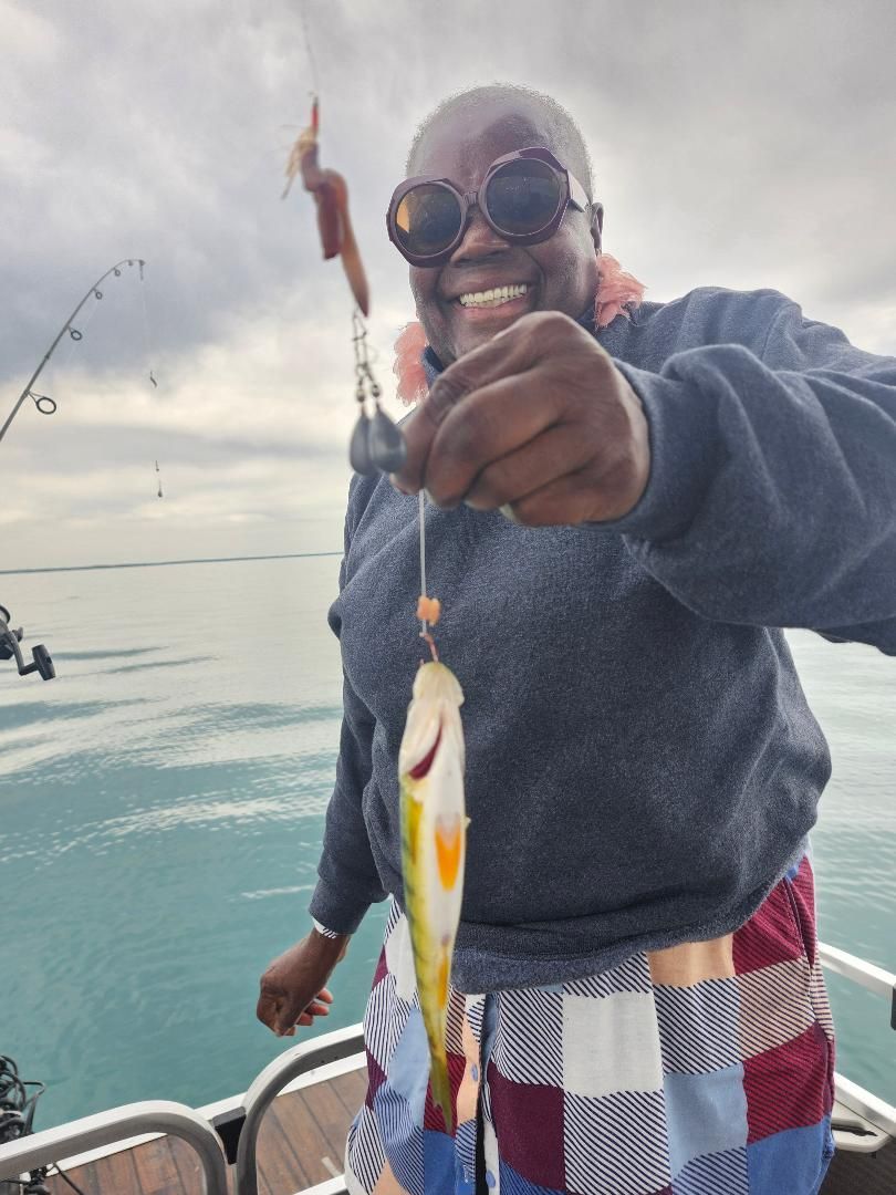 Person holding a small fish up on a fishing line, smiling near water.