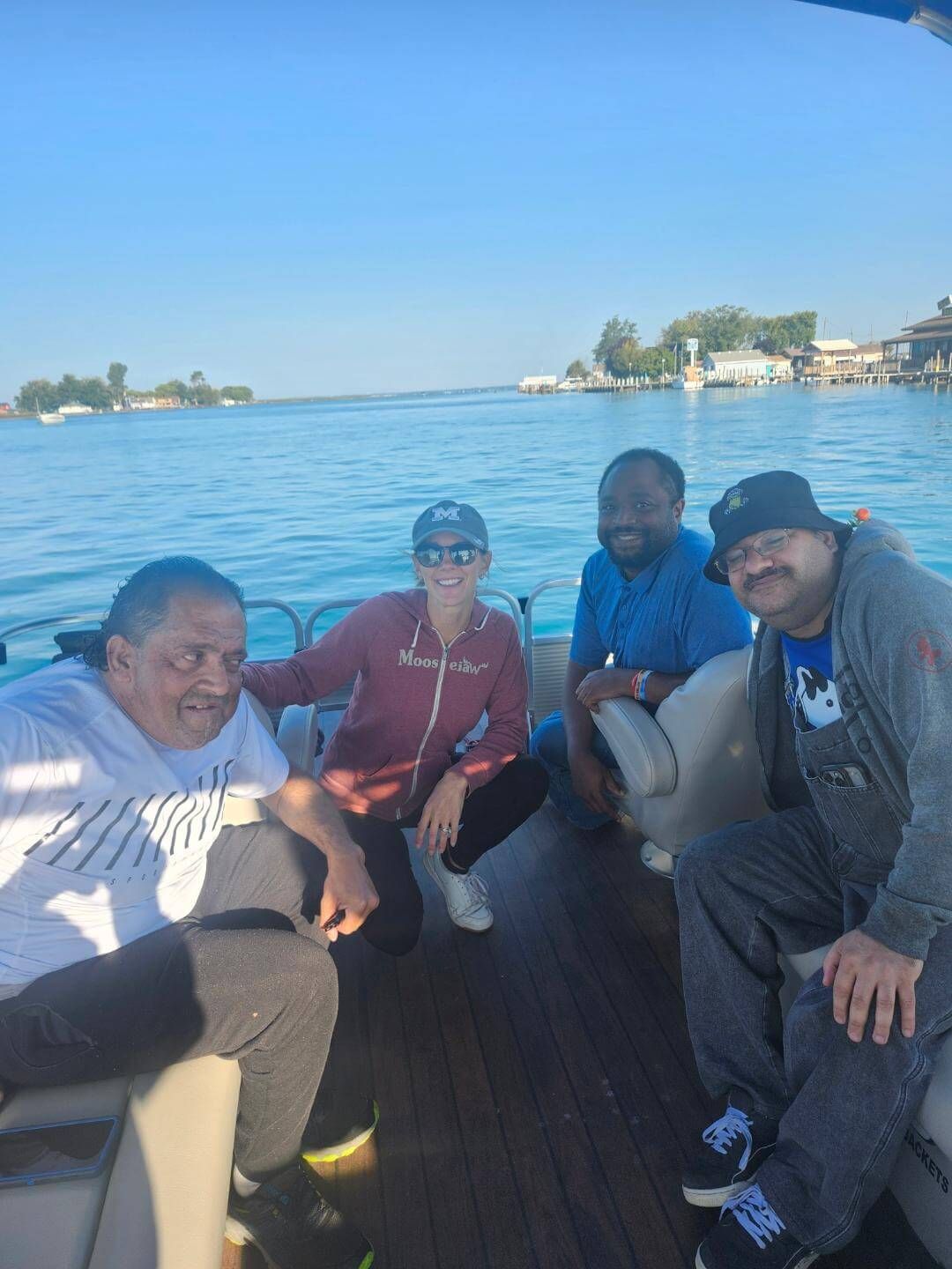 Four people on a boat on the water; two are sitting and two are squatting, with buildings in the background.