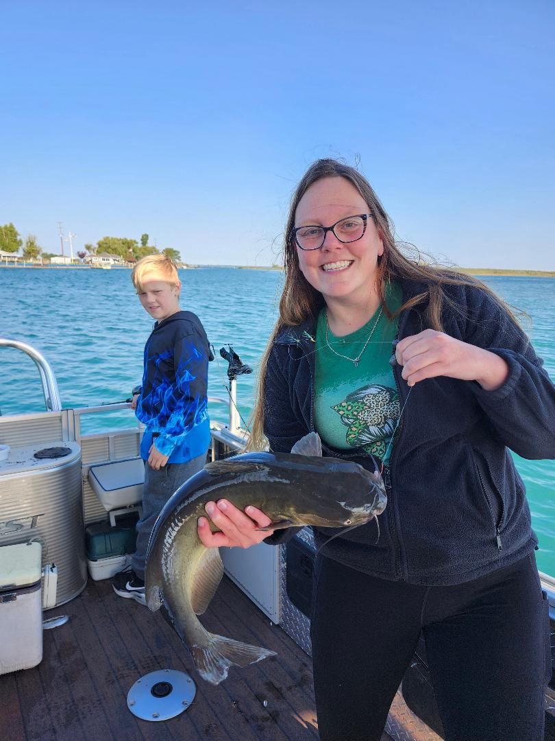 Woman holding a large fish on a boat, smiling. A child fishes nearby on a sunny day.