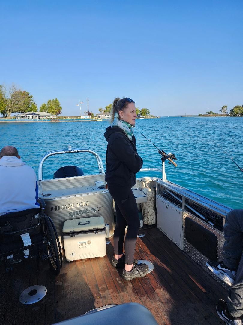 Woman fishing from a boat on a sunny day. She wears a black jacket and pants. Blue water and sky.