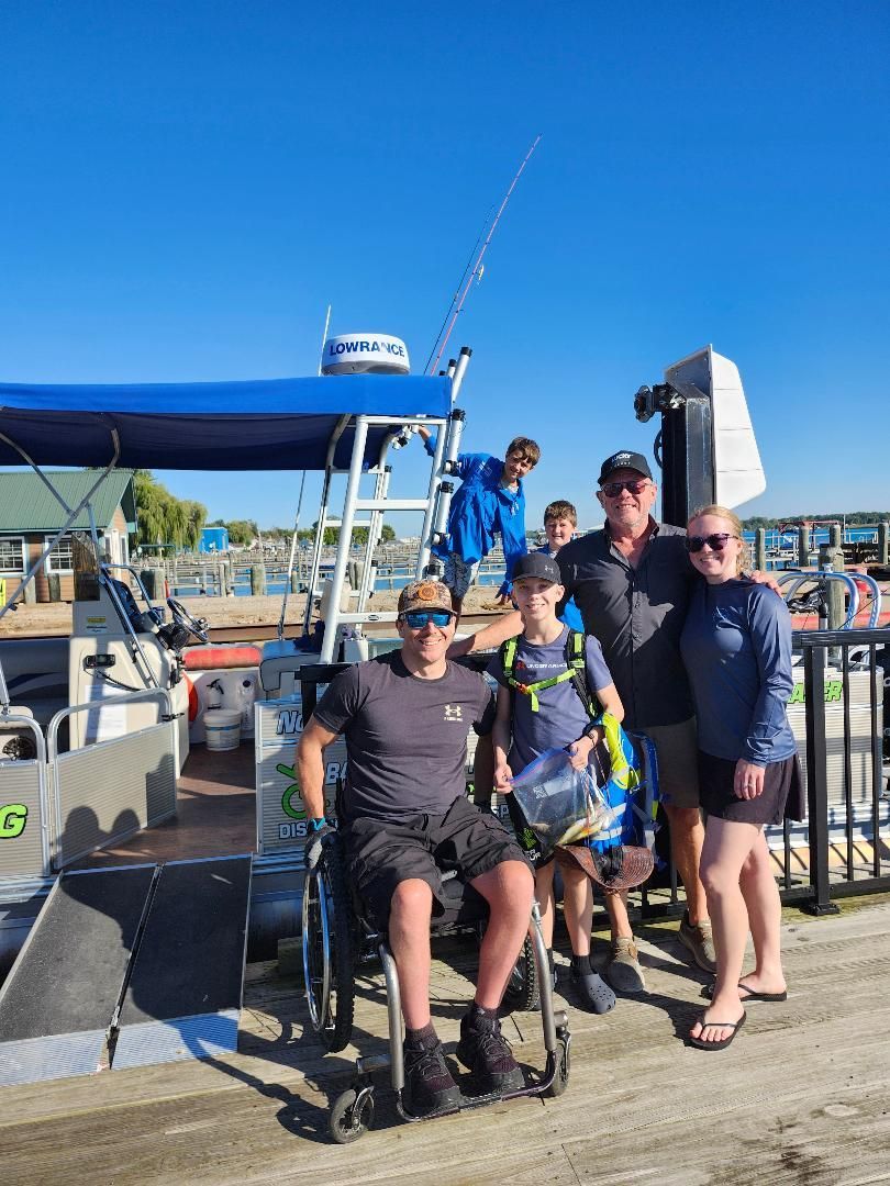 Family on a boat dock, one in wheelchair. Fishing rod up, blue sky.