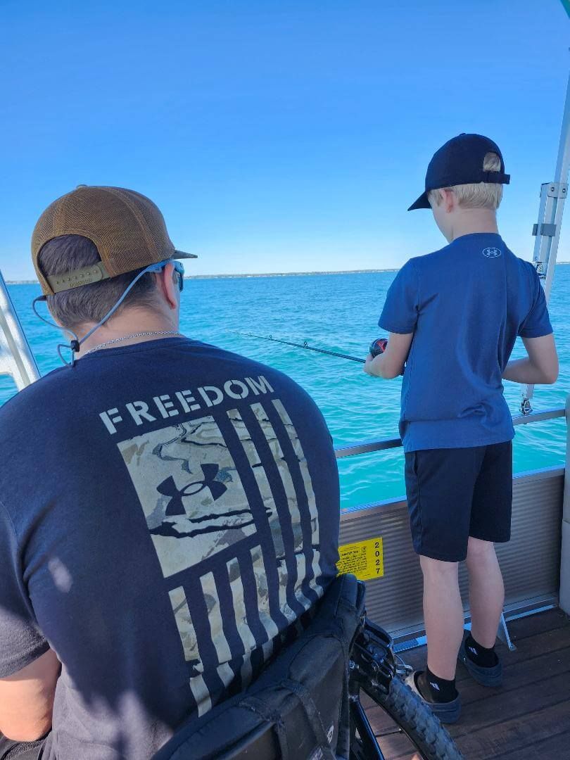 Man in a wheelchair and child fishing from a boat on a sunny day.