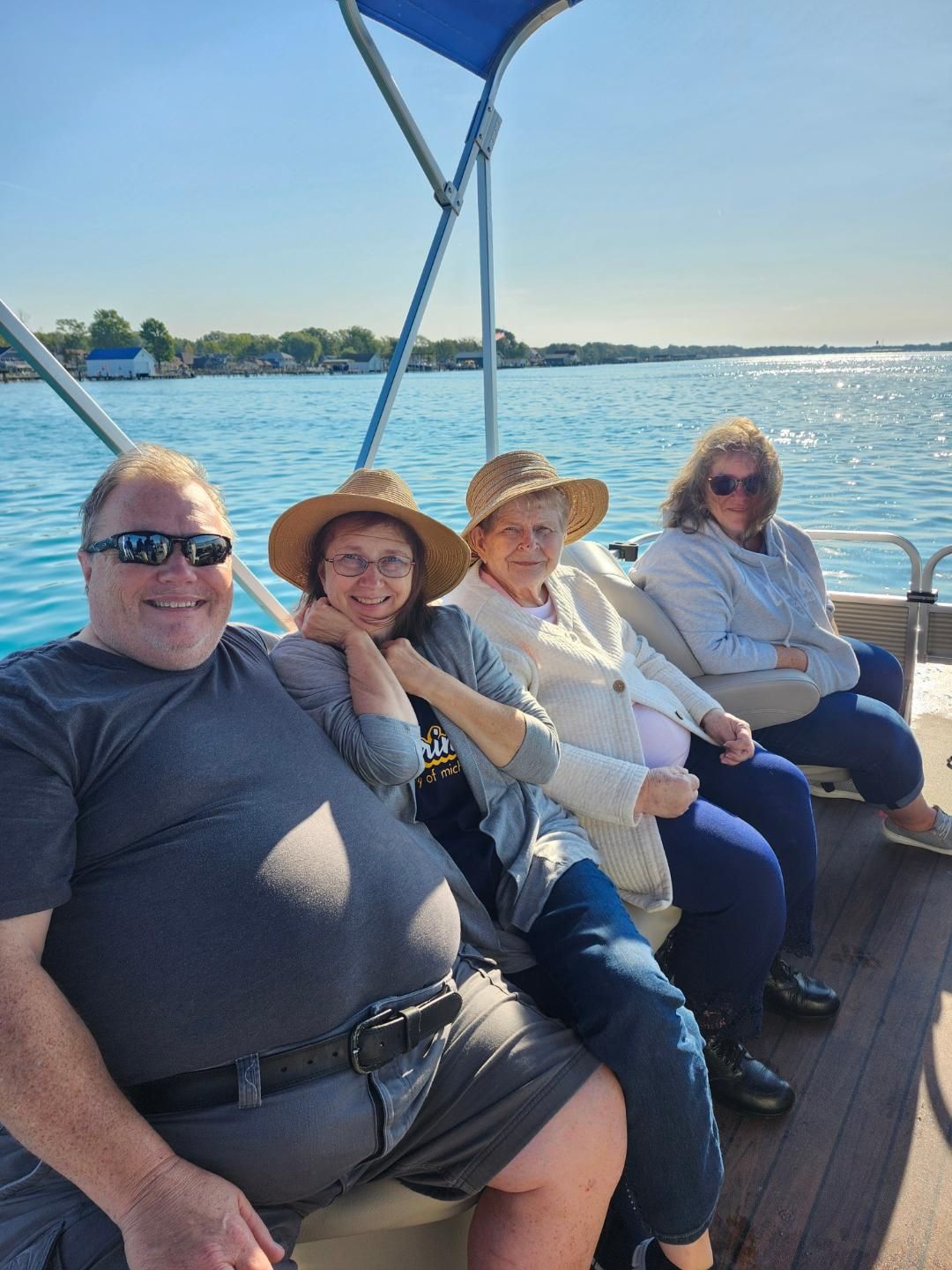 Four people on a boat, smiling in the sunlight. Lake visible.