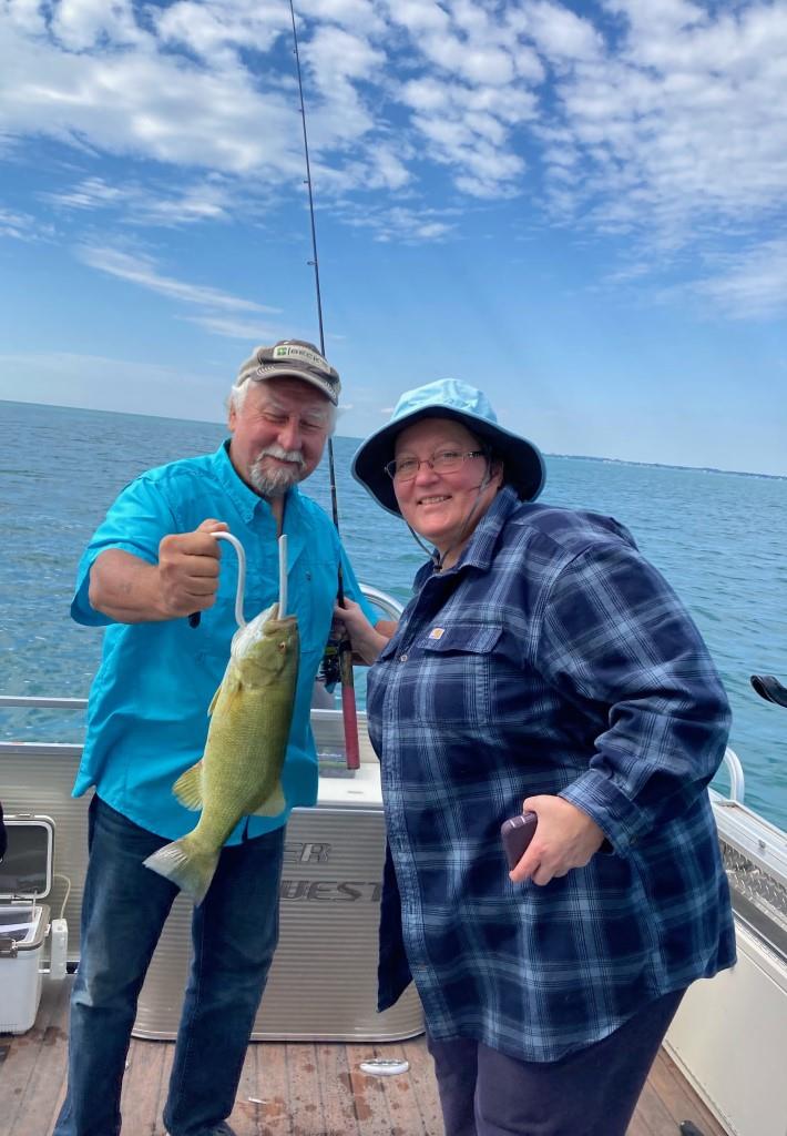 A man and a woman are standing on a boat holding a fish.