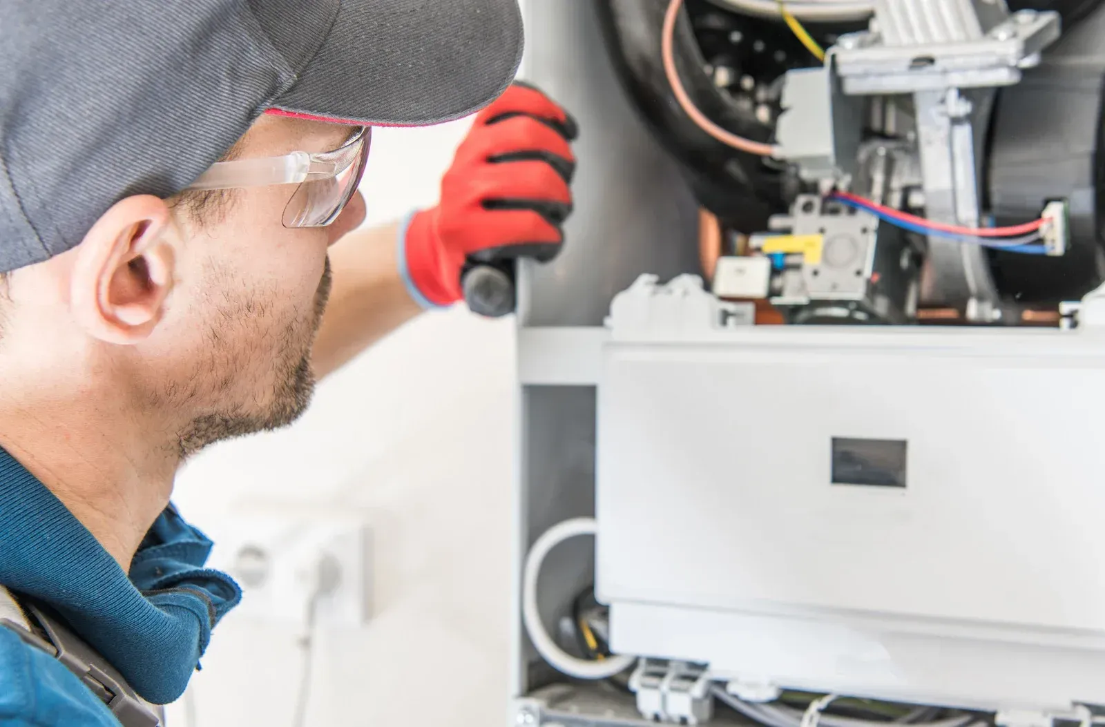 A technician wearing safety glasses and gloves works on a furnace.