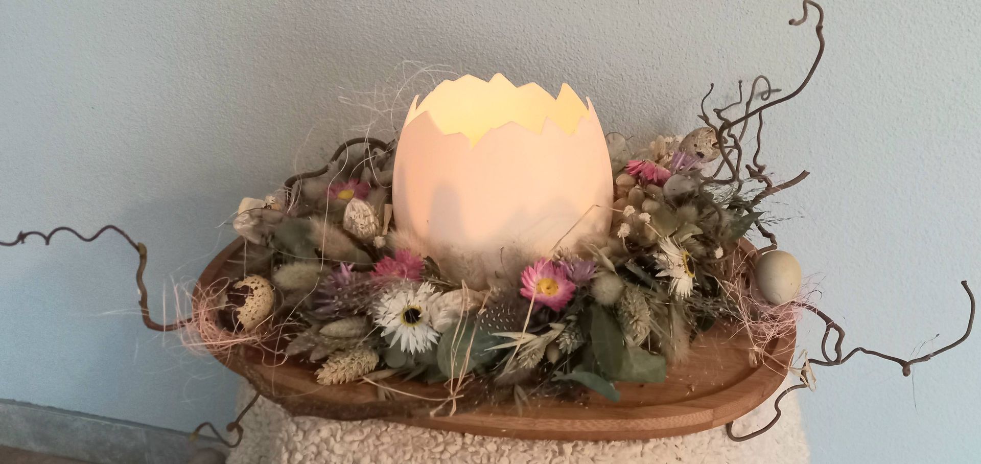 Paasstuk op schaal, 
Dit is een ’ei’catcher op je tafel. In het grote ei kan een lichtje. Het kransje wordt gemaakt met eucalypthus en droogbloemen. De kronkeltakken passen precies bij de a-symetrische vorm van de houten schaal.