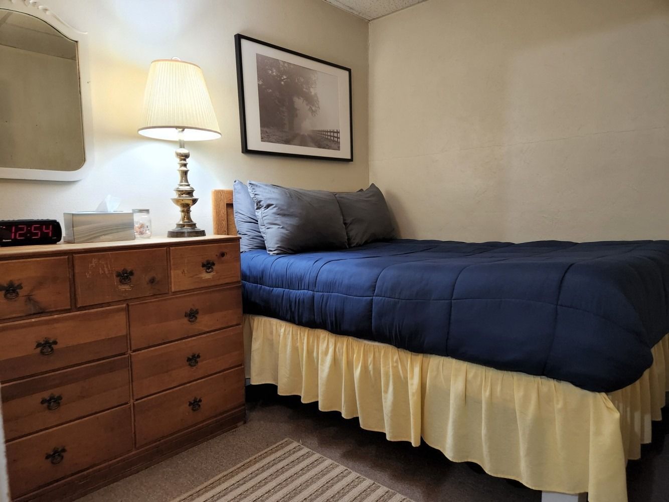 A bedroom with a bed , dresser , lamp and mirror.