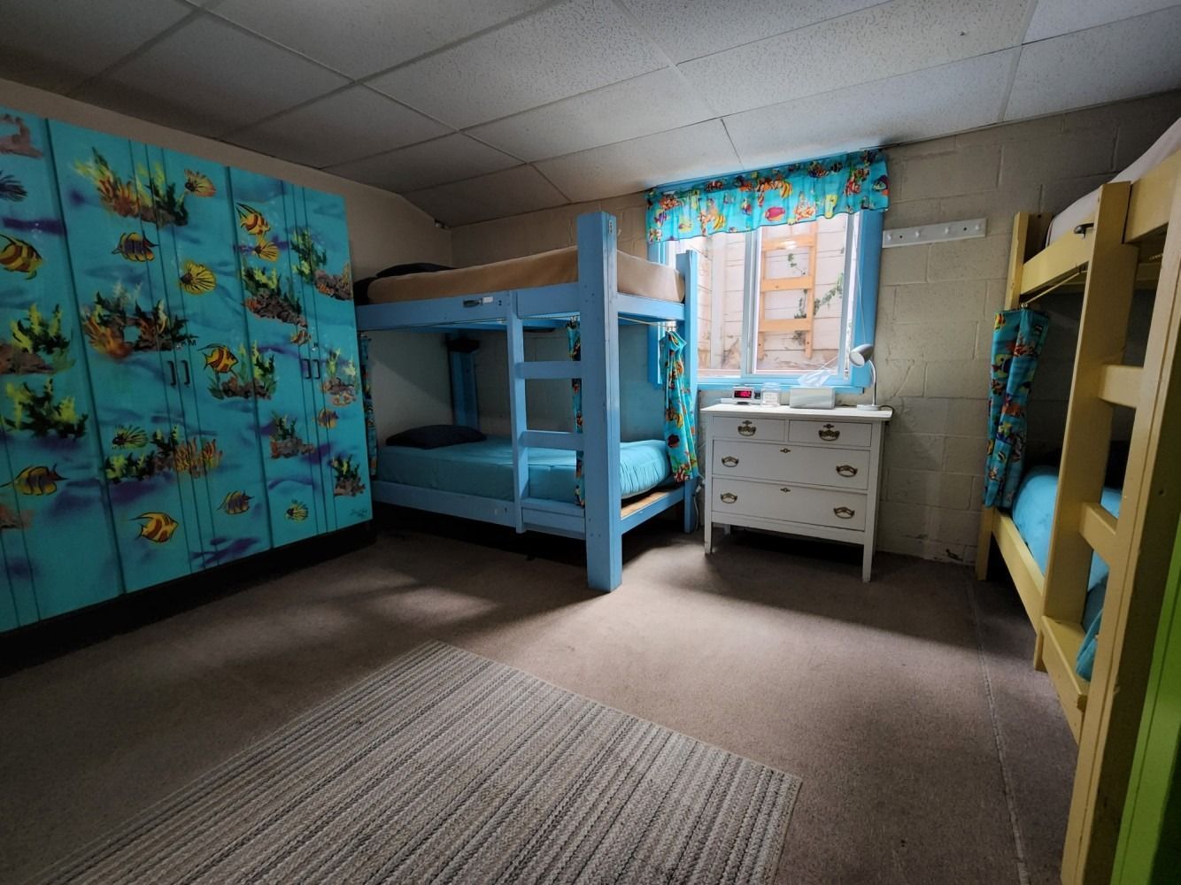 A bedroom with bunk beds , a dresser and a window.