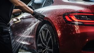 A man is hand washing a red car with a hose.