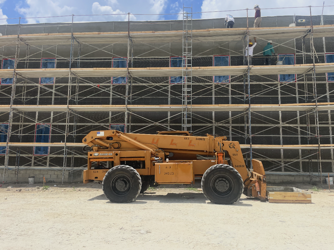 Orange construction lift in front of a scaffolded building under construction