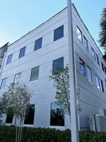 Modern white office building with blue windows and small trees outside